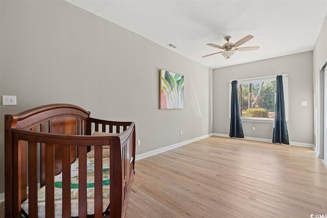 bedroom with baseboards, a nursery area, a ceiling fan, and light wood finished floors