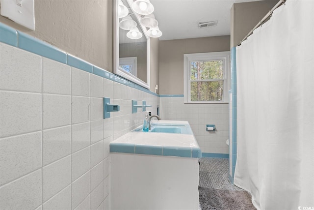 full bath with visible vents, vanity, wainscoting, tile walls, and a shower with curtain