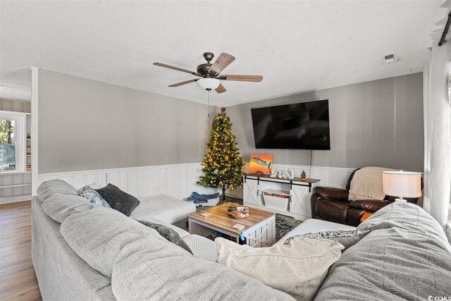living area with a wainscoted wall, ceiling fan, wood finished floors, and visible vents