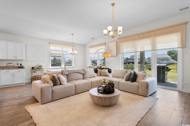 living area with a chandelier, lofted ceiling, visible vents, and light wood-type flooring