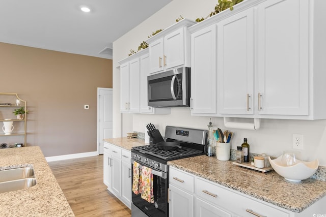 kitchen with light stone countertops, white cabinetry, baseboards, stainless steel appliances, and light wood-style flooring