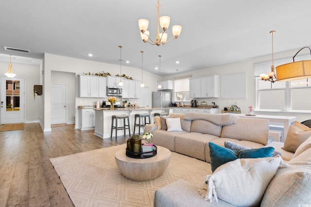 living area featuring light wood-style floors, visible vents, recessed lighting, and a notable chandelier