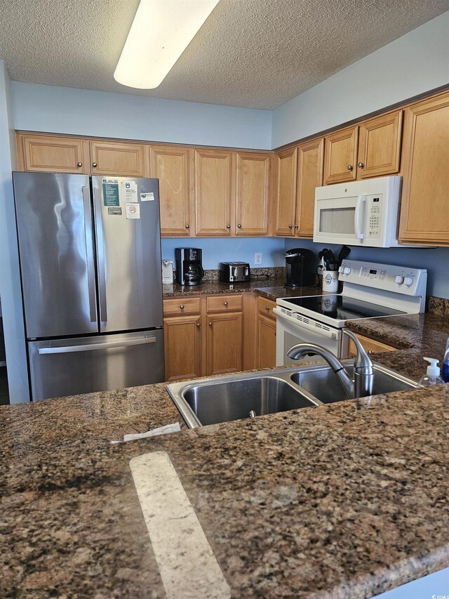 kitchen featuring white appliances, a textured ceiling, and a sink