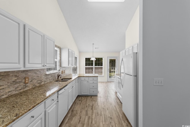 kitchen with a sink, light wood finished floors, a peninsula, white appliances, and white cabinetry