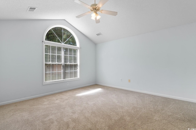 carpeted empty room with baseboards, ceiling fan, vaulted ceiling, and visible vents