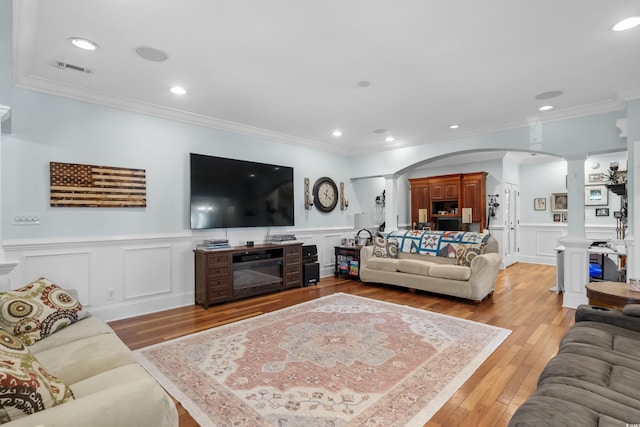 living area featuring crown molding, light wood-type flooring, ornate columns, and arched walkways