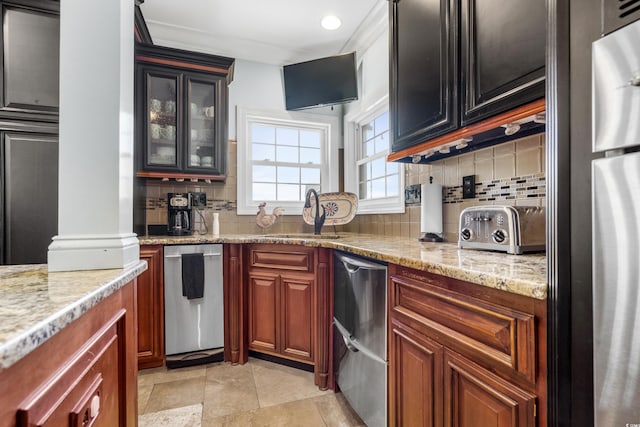 kitchen with a sink, tasteful backsplash, light stone counters, glass insert cabinets, and appliances with stainless steel finishes