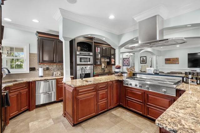 kitchen with island exhaust hood, ornate columns, a sink, stainless steel appliances, and decorative backsplash