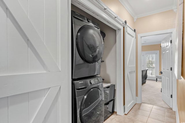 clothes washing area featuring stacked washer / dryer, a barn door, light tile patterned floors, crown molding, and laundry area