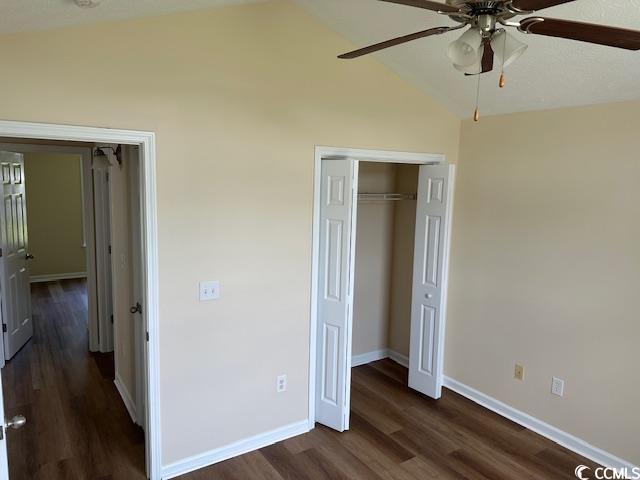 unfurnished bedroom with a ceiling fan, baseboards, lofted ceiling, dark wood-type flooring, and a closet