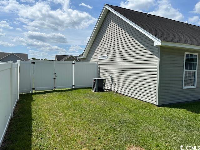 view of side of home with fence, central AC unit, a lawn, and roof with shingles