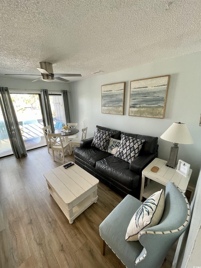 living room with a textured ceiling, ceiling fan, and wood finished floors