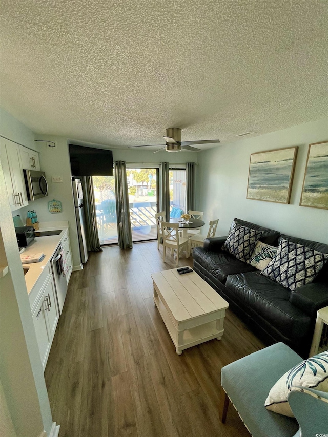 living room featuring a ceiling fan, a textured ceiling, and dark wood-type flooring