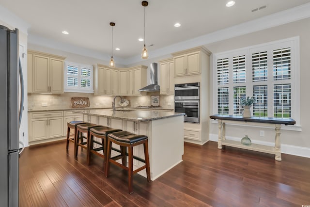 kitchen featuring wall chimney range hood, visible vents, appliances with stainless steel finishes, cream cabinets, and light stone counters