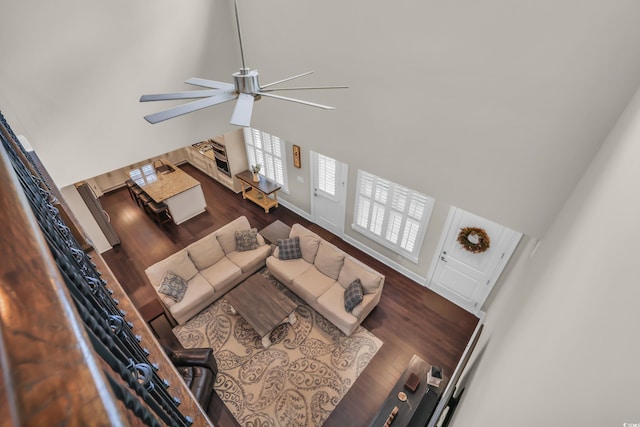 living room with baseboards, a ceiling fan, dark wood-style flooring, and a towering ceiling