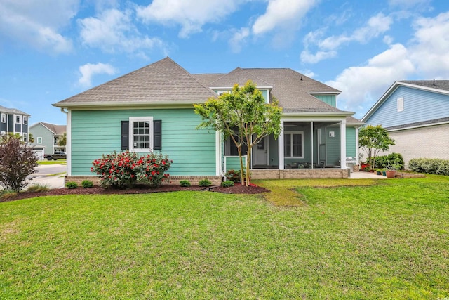 view of front of home featuring roof with shingles, a front yard, and a sunroom