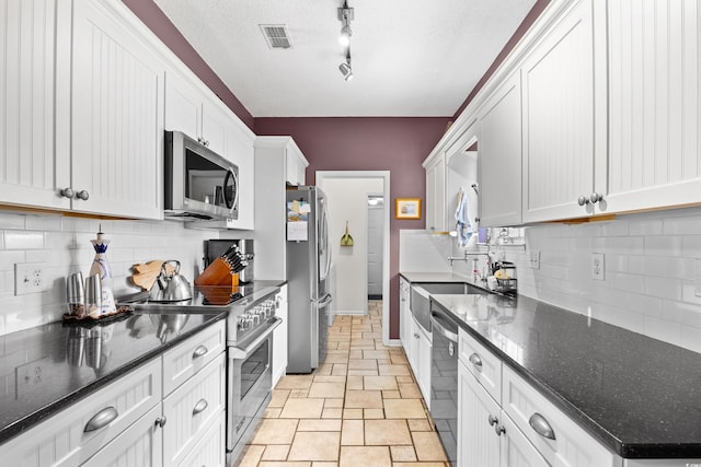 kitchen featuring a sink, stainless steel appliances, white cabinetry, stone finish flooring, and backsplash