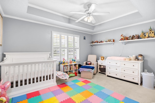 bedroom featuring crown molding, a nursery area, carpet flooring, a raised ceiling, and a ceiling fan