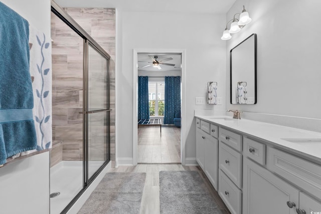 bathroom featuring ceiling fan, a sink, double vanity, baseboards, and a shower stall