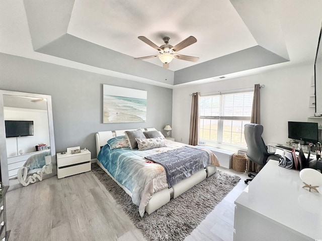 bedroom featuring a ceiling fan, a tray ceiling, and light wood-type flooring