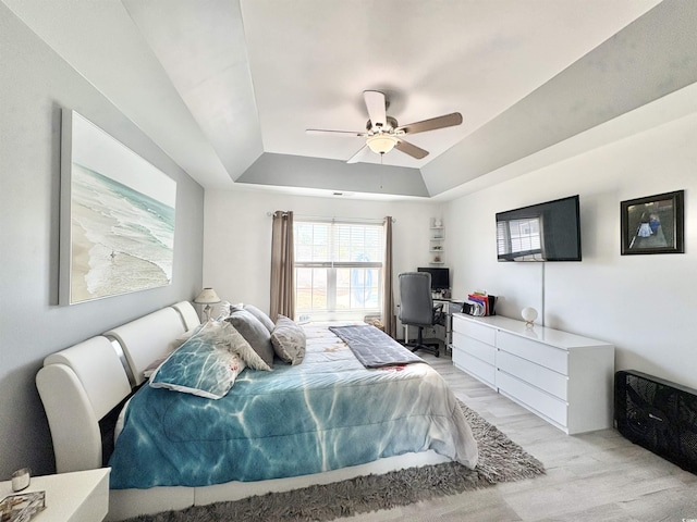 bedroom featuring light wood-style flooring, a raised ceiling, and ceiling fan