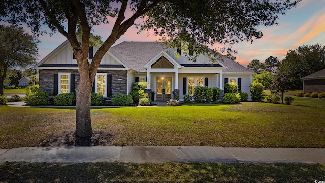 view of front of home featuring board and batten siding, stone siding, french doors, and a front yard