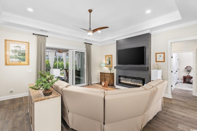 living area featuring dark wood-style flooring, baseboards, a raised ceiling, a large fireplace, and a ceiling fan