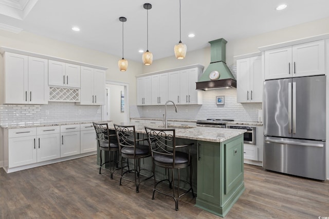 kitchen with a kitchen island with sink, stainless steel appliances, white cabinetry, decorative backsplash, and custom range hood