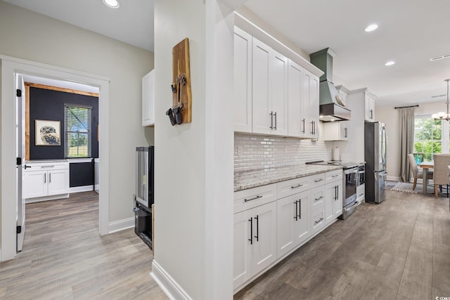 kitchen with white cabinets, tasteful backsplash, custom range hood, light wood finished floors, and appliances with stainless steel finishes