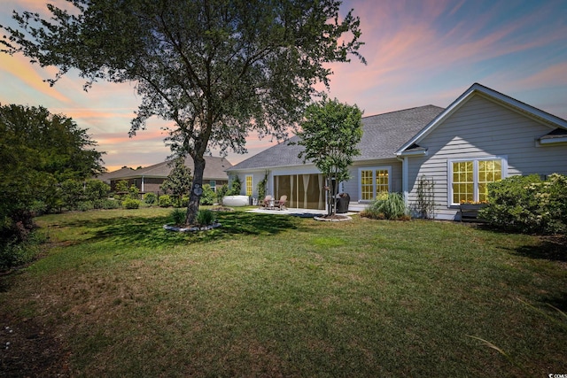 rear view of house with a yard, a patio, and a shingled roof