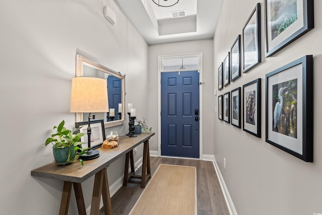 doorway featuring baseboards, dark wood-style flooring, a raised ceiling, and visible vents