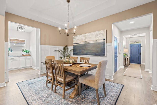 dining space with a notable chandelier, wainscoting, a raised ceiling, a decorative wall, and light wood-style floors