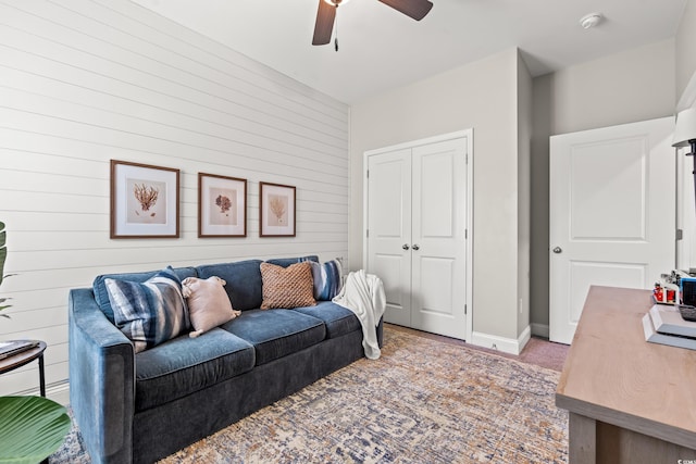 living area featuring wooden walls, a ceiling fan, baseboards, and light carpet