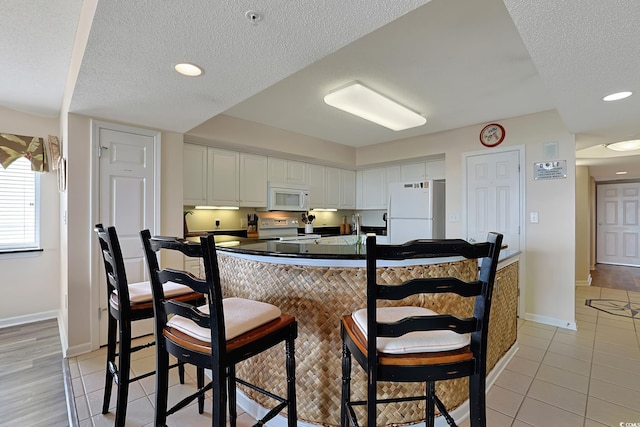 kitchen featuring dark countertops, white appliances, white cabinetry, baseboards, and light tile patterned floors