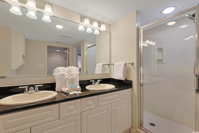 bathroom featuring a sink, double vanity, a shower stall, and a textured ceiling
