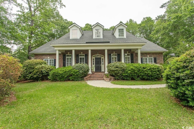 cape cod home with brick siding, a shingled roof, covered porch, and a front yard