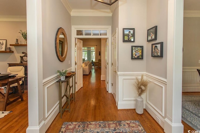 hall with a decorative wall, ornamental molding, wood finished floors, and a wainscoted wall