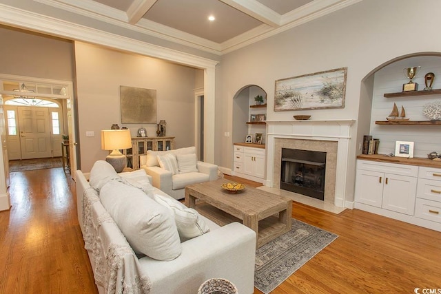 living room with ornamental molding, beam ceiling, built in shelves, a fireplace with flush hearth, and light wood finished floors