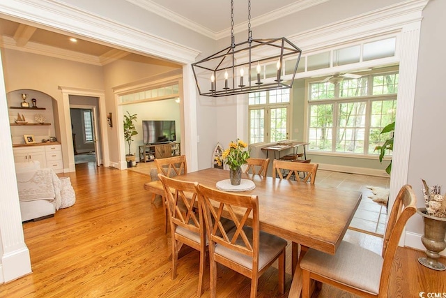 dining area with crown molding, an inviting chandelier, light wood-style floors, and built in shelves