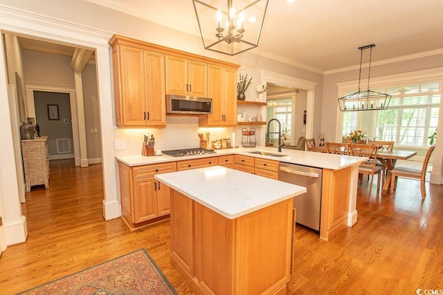 kitchen featuring appliances with stainless steel finishes, a sink, light countertops, a peninsula, and a notable chandelier