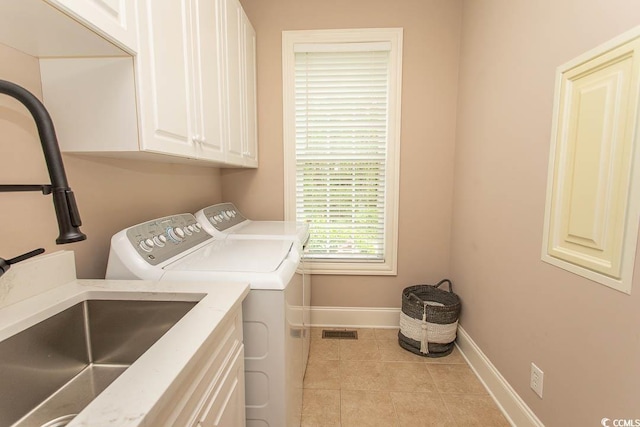 clothes washing area featuring washing machine and dryer, baseboards, a sink, cabinet space, and light tile patterned floors