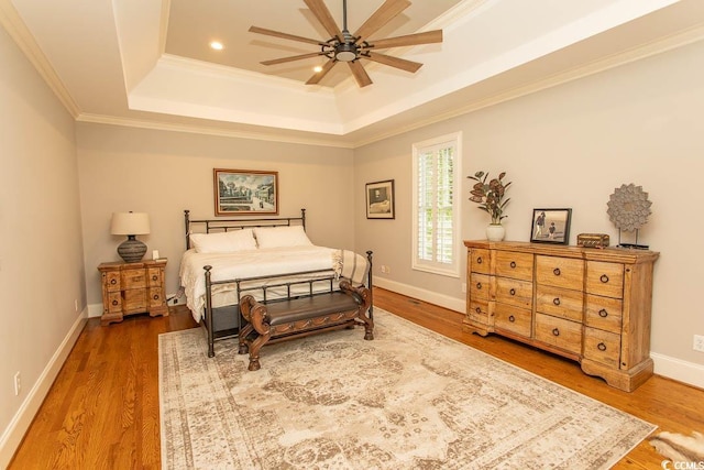 bedroom featuring baseboards, ornamental molding, wood finished floors, and a raised ceiling