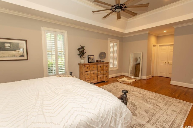 bedroom with ceiling fan, wood finished floors, baseboards, ornamental molding, and a tray ceiling