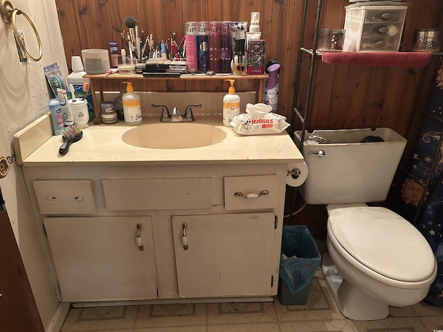 half bath featuring wooden walls, toilet, tile patterned floors, and vanity