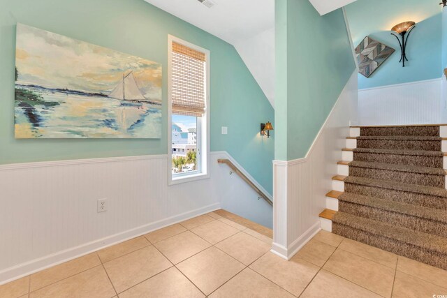 2808 N Ocean Blvd, North Myrtle Beach, SC 29582 - staircase featuring tile patterned floors, a wainscoted wall, and vaulted ceiling