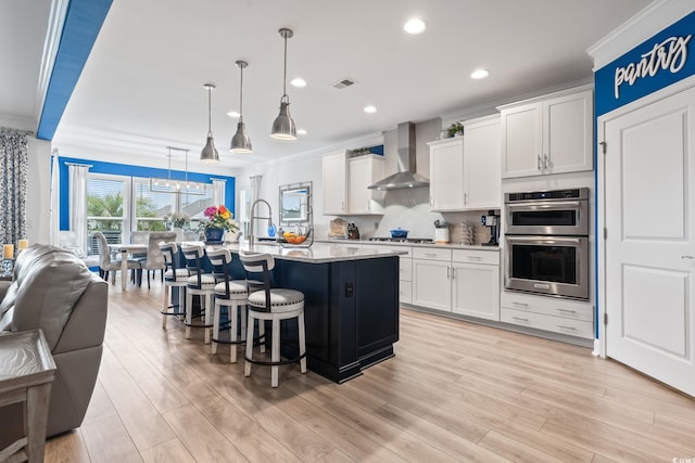 kitchen featuring wall chimney range hood, crown molding, visible vents, and open floor plan