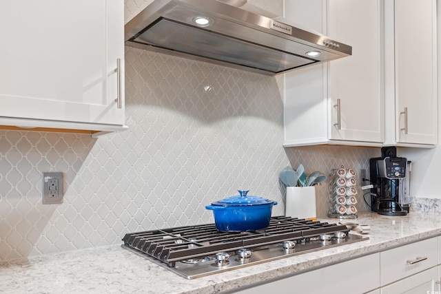 kitchen with decorative backsplash, stainless steel gas cooktop, light stone counters, white cabinets, and extractor fan