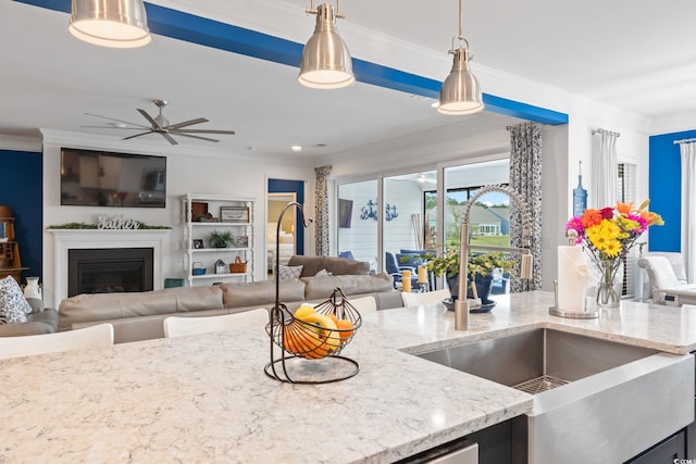 kitchen with light stone counters, ornamental molding, a ceiling fan, open floor plan, and pendant lighting
