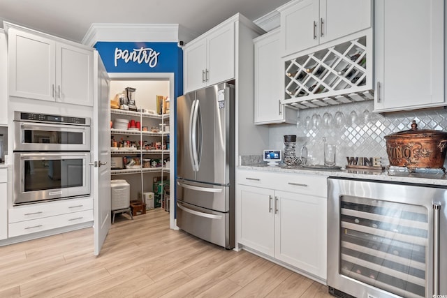 kitchen featuring appliances with stainless steel finishes, tasteful backsplash, light wood-type flooring, white cabinets, and wine cooler