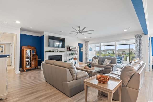 living area featuring a ceiling fan, visible vents, a fireplace, light wood finished floors, and ornamental molding